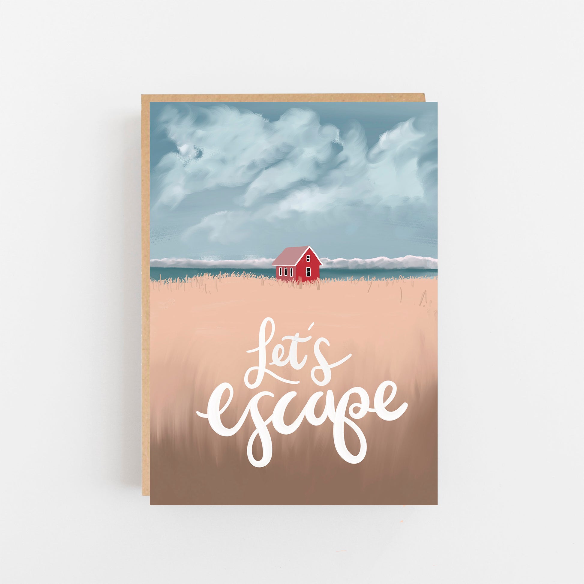 Greeting card with the words Let's Escape on the front in white background pale beige field with a small terracota house in the background with the sea and sky of clouds behind this. brown kraft envelope