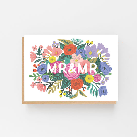 Wedding Card with the words MR & MRS in white in the middle of the card which is displayed landscaped . the words are surrounded by multi coloured flowers. Brown Kraft envelope.