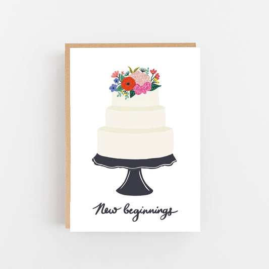 Wedding Card white background with a cake on a black cake stand bunch of flowers on top of the cake underneath the cake stand the words new beginnings in Black. Brown Kraft envelope.