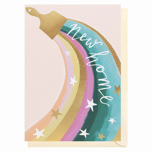 New Home card with the words new hoe in white coming out of ag old foil paint brush with pastel colours coming down from the paint brush with gold stars on the top of the pastel colour. Pale beige Envelope  and background to the card