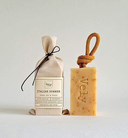 cream soap with dark orange rope and the word Vely etched into the bar. the fragrance is Italian Summer. The hessian bag that the soap comes in is shown to the left of the soap.