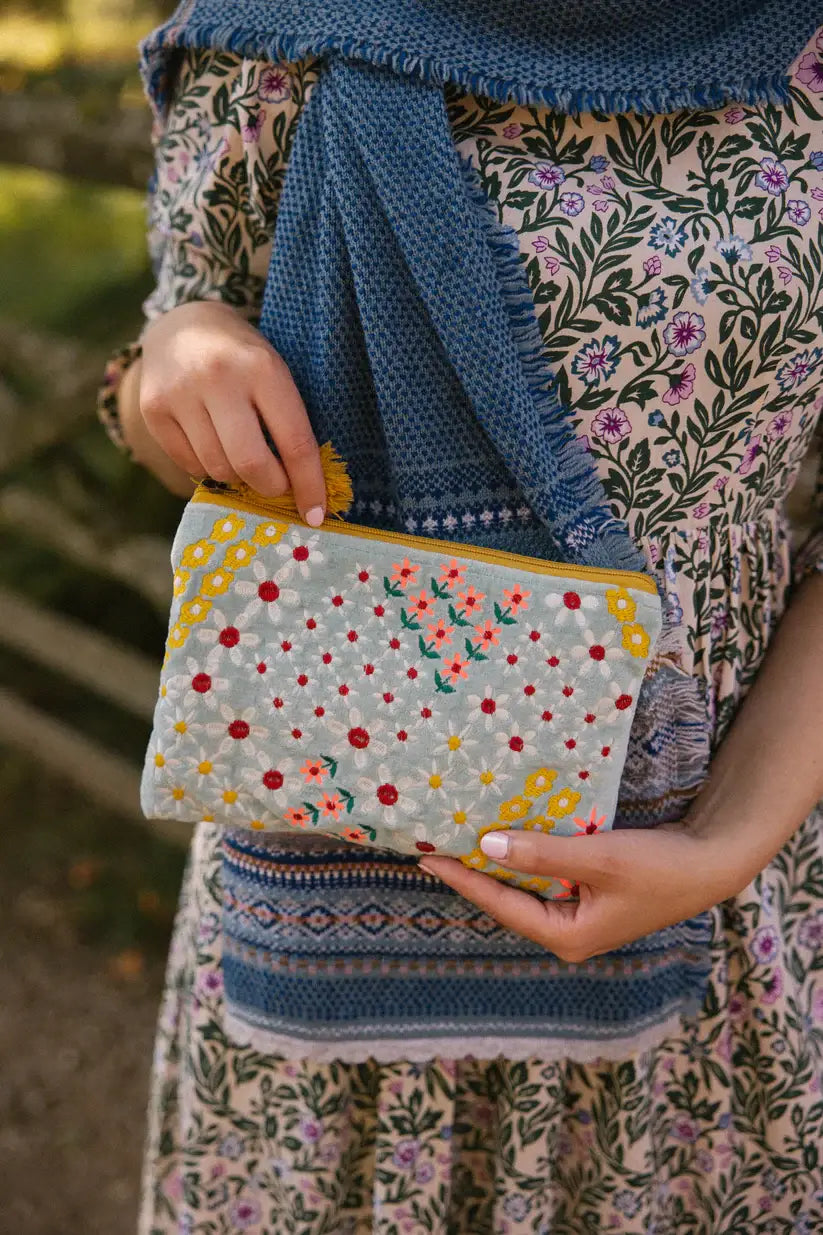 medium size pouch in pale blue velvet type material with white with red centres yellow and  pink flowers embroidered on the front with mustard coloured zip and tassel on the end.