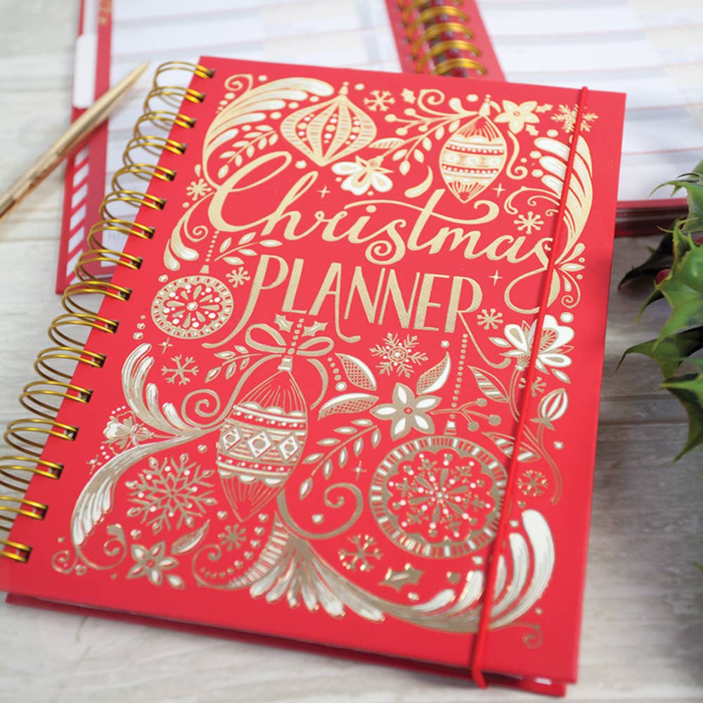 Gold spiral bound red book with gold decorations on the cover and written in gold it states Christmas Planner . There is a piece of red elastic around the right handside of the book.