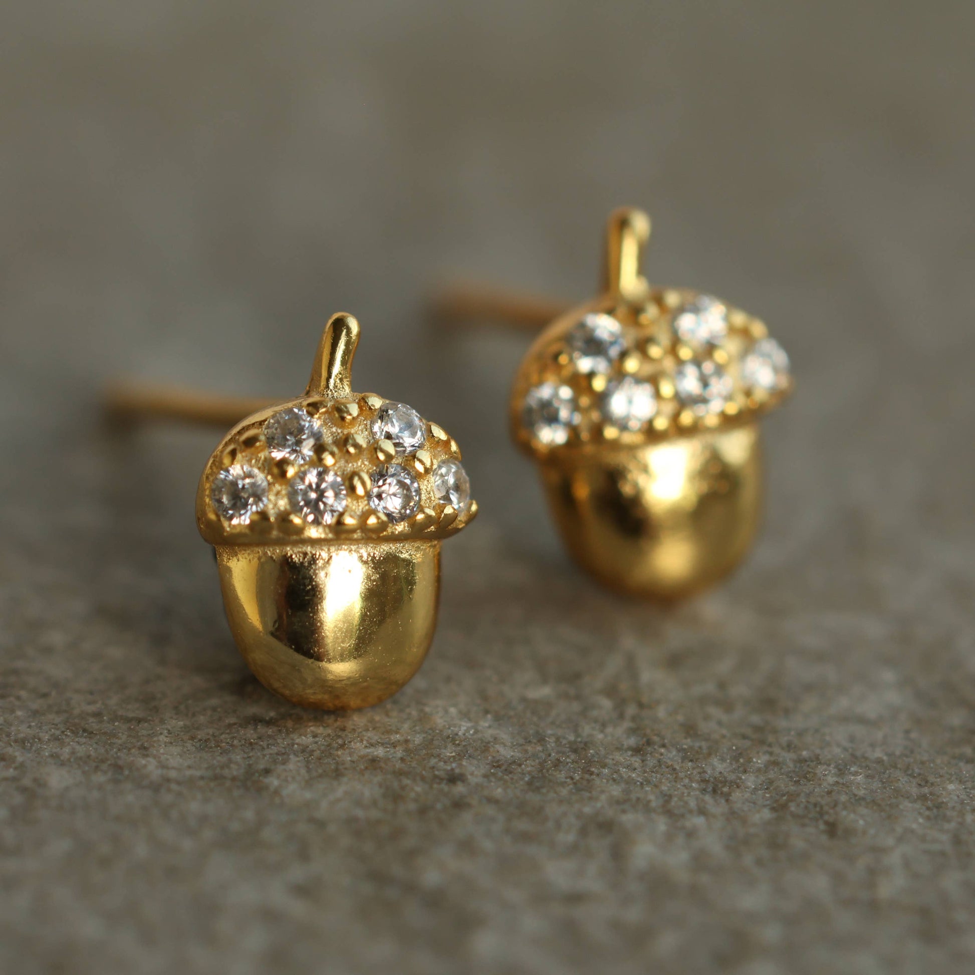 close up image of a pair of brass acorn shaped earrings with crystal tops 