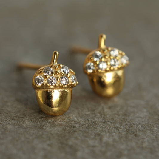close up image of a pair of brass acorn shaped earrings with crystal tops 