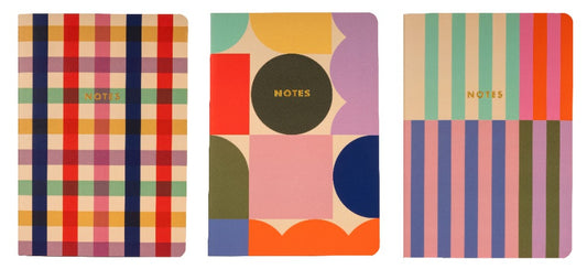 image shows 3 notebooks each with the word NOTES embossed in gold foil  on the front of each book. each book has a different  cover pattern using the same colours of pink, red, navy,brown, yellow and lilac.  