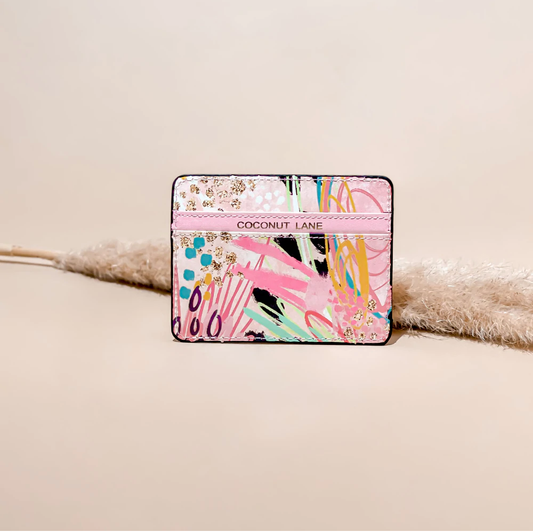 mage shows a card holder with 2 sections for cards. the middle section has coconut lane embossed in gold foil across it. the design is abstract but mainly shows various pinks with a splash of black and turquoise.