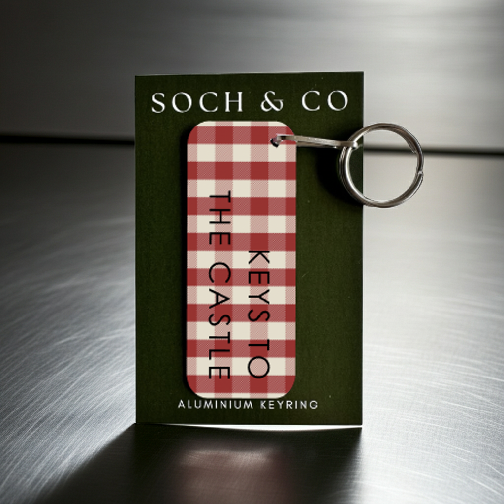Red and white checkered keyring with 'The Castle' text in a Soch & Co packaging on a reflective surface.